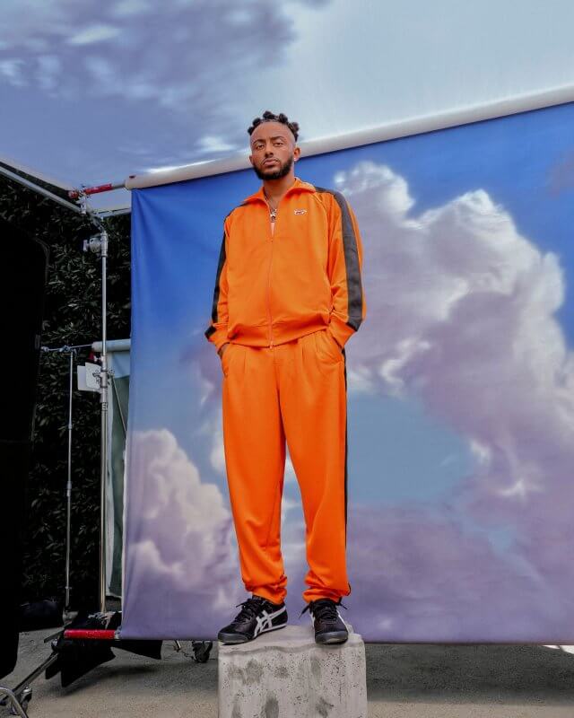 Aminé stands on a concrete box on set for L’Officiel photographed by Steven Taylor